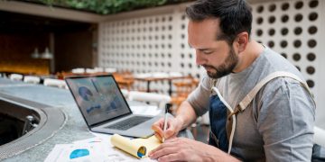 Portrait of a male business owner doing the books at a restaurant using a laptop computer. Design on screen was made from scratch by us.