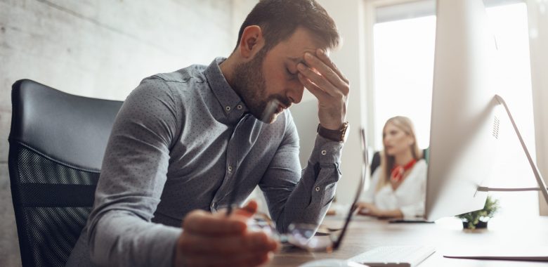 Young handsome frustrated and stressed businessman sitting at the office front a computer and holding head.