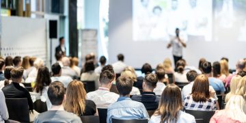 Audience at the conference hall. Male speaker giving a talk in conference hall at business event. Business and Entrepreneurship concept. Focus on unrecognizable people in audience.