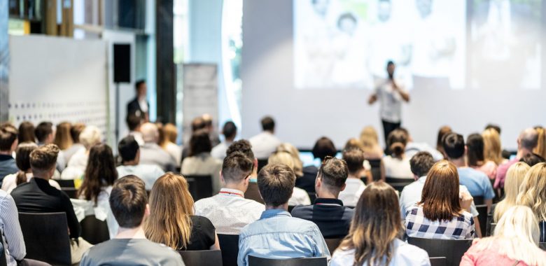 Audience at the conference hall. Male speaker giving a talk in conference hall at business event. Business and Entrepreneurship concept. Focus on unrecognizable people in audience.